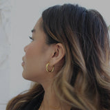 image of a woman wearing gold twisted hoops looking off to the side