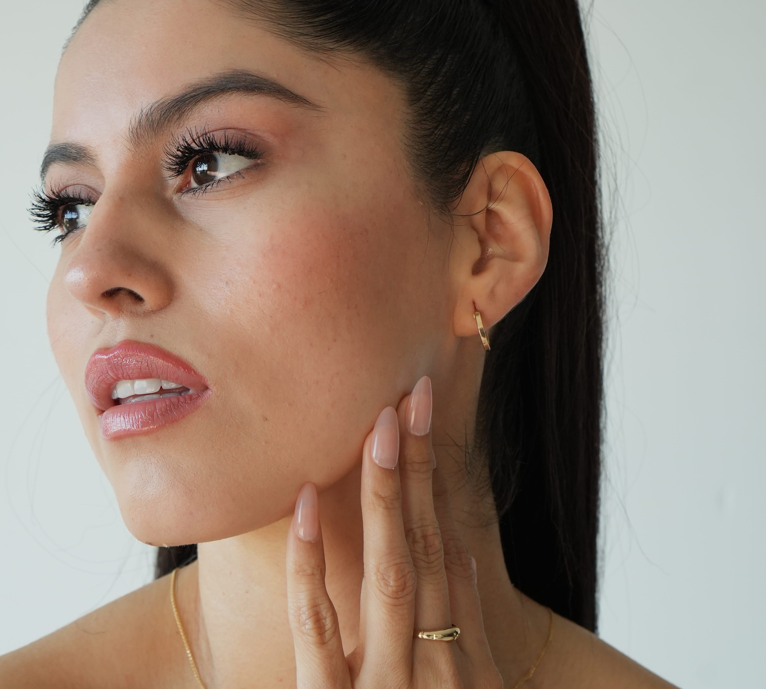 Woman with a high ponytail touching her face against a plain background
