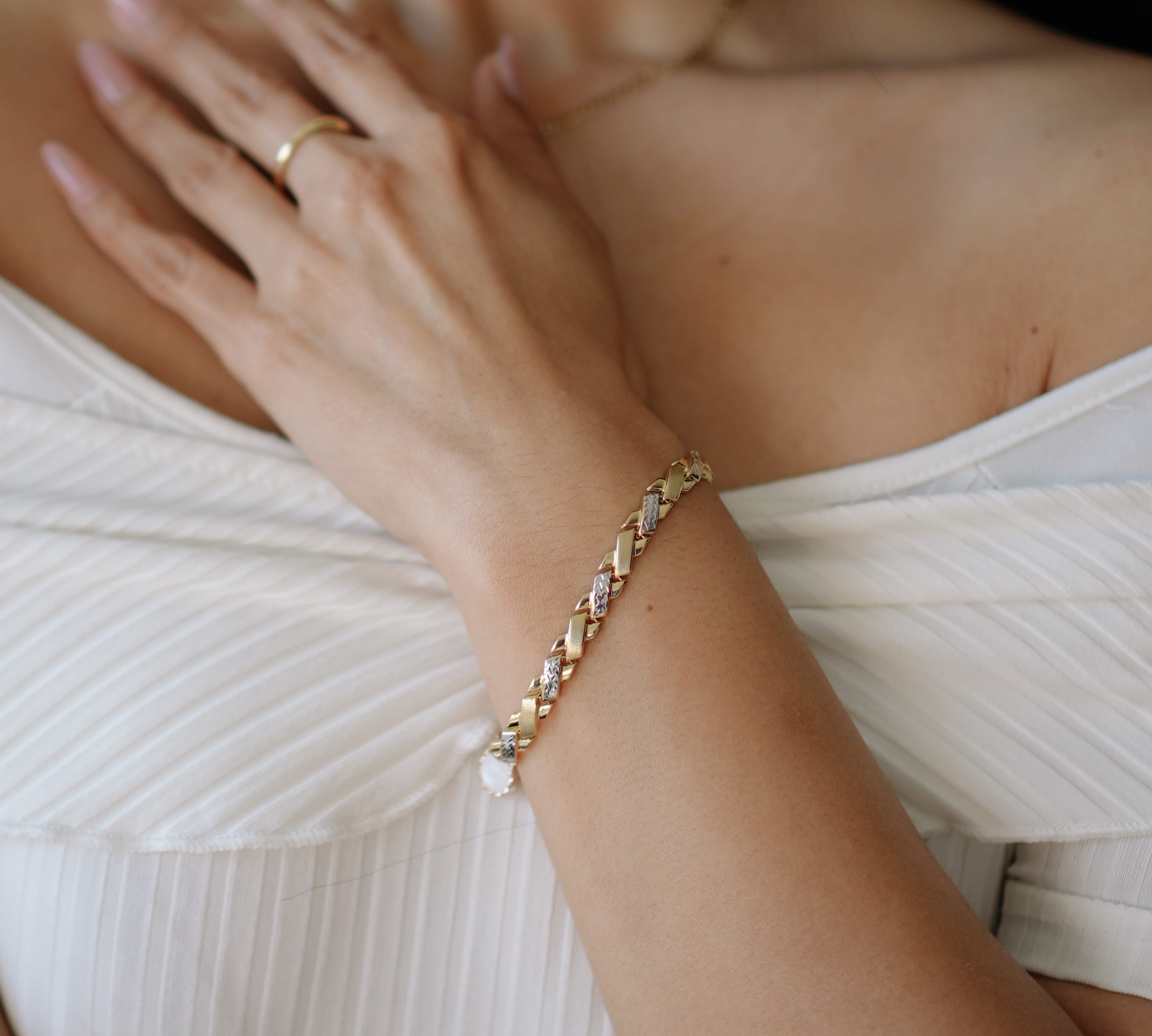 Close-up of a person wearing a gold bracelet and ring on a white background
