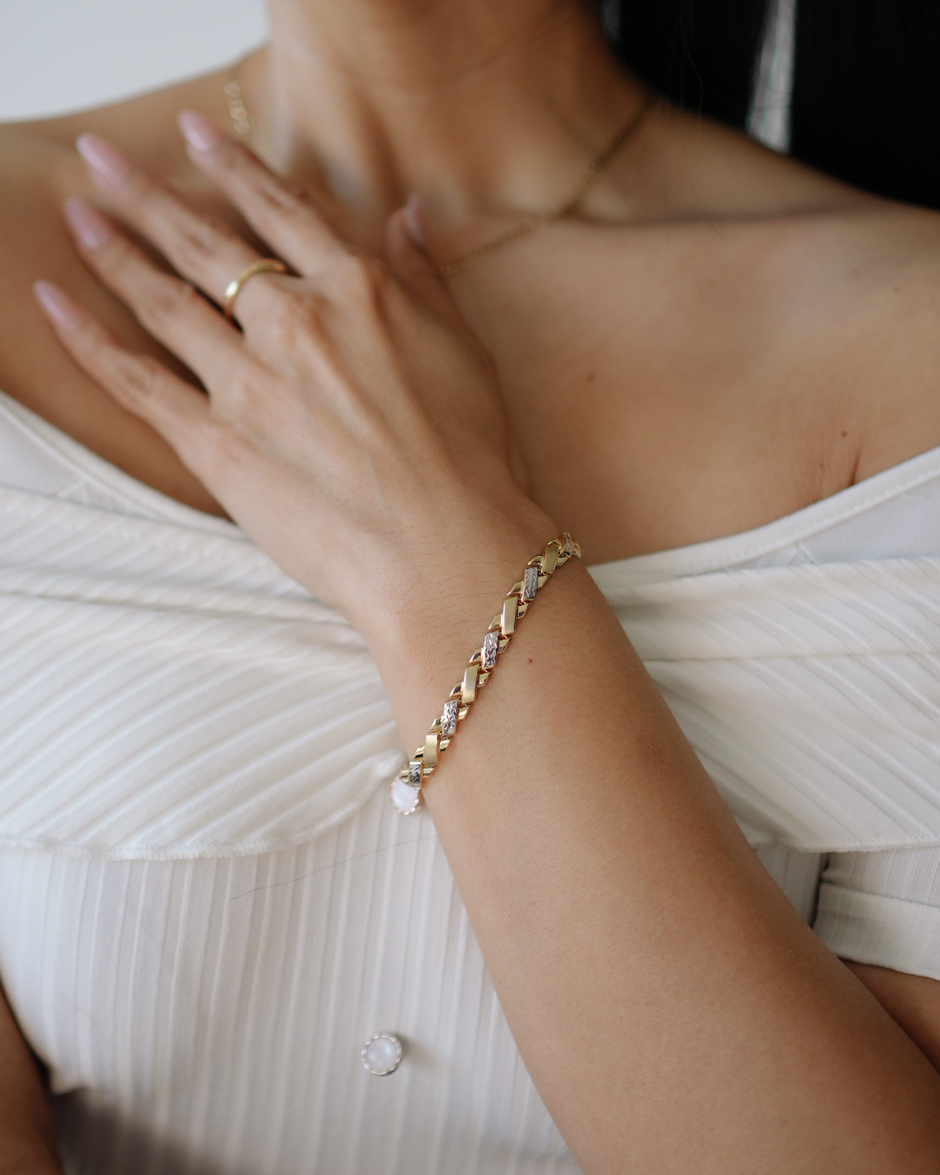 Close-up of a person wearing a gold bracelet and ring on a white background