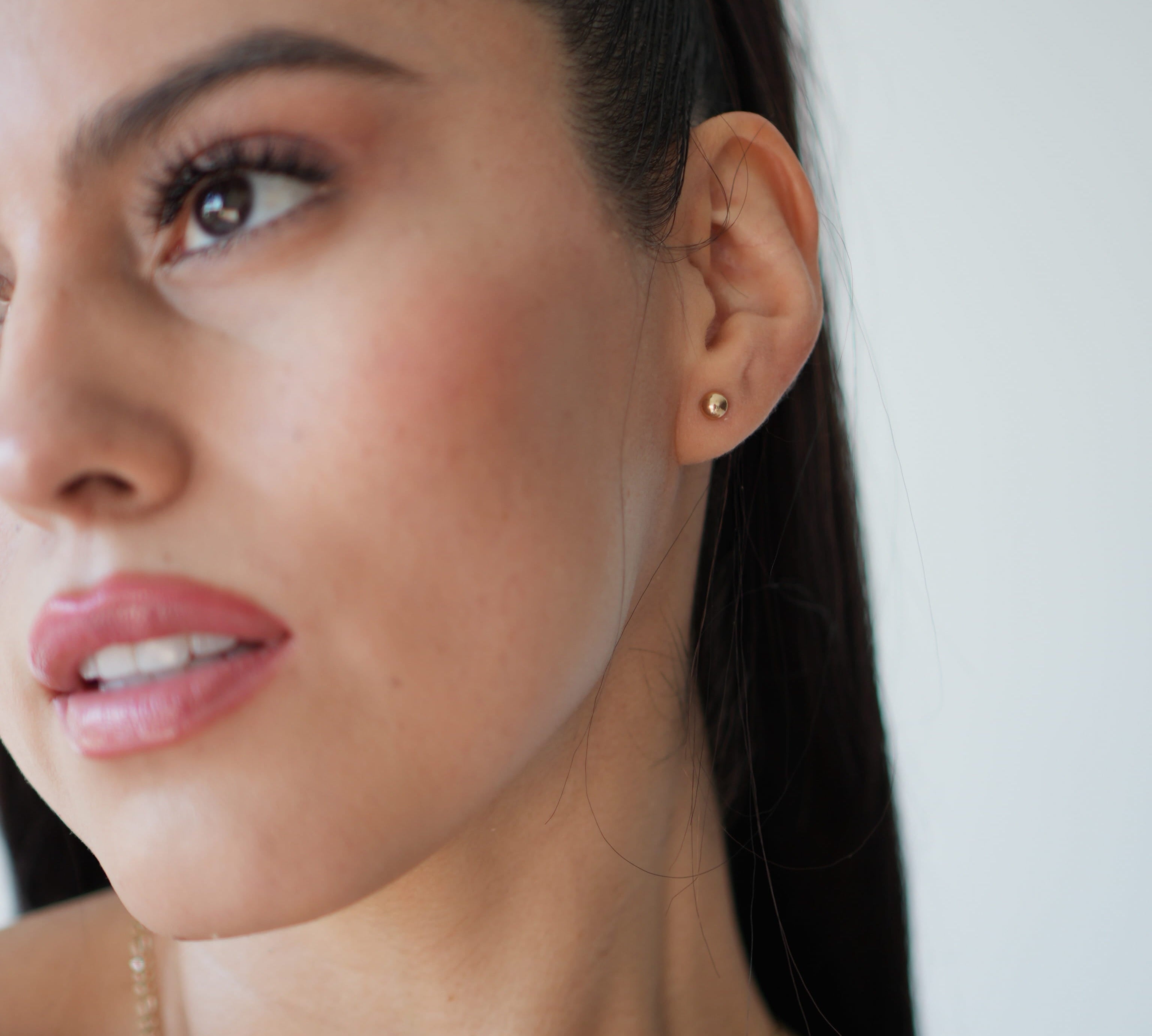 Close-up of a woman wearing a gold earring and necklace against a neutral background