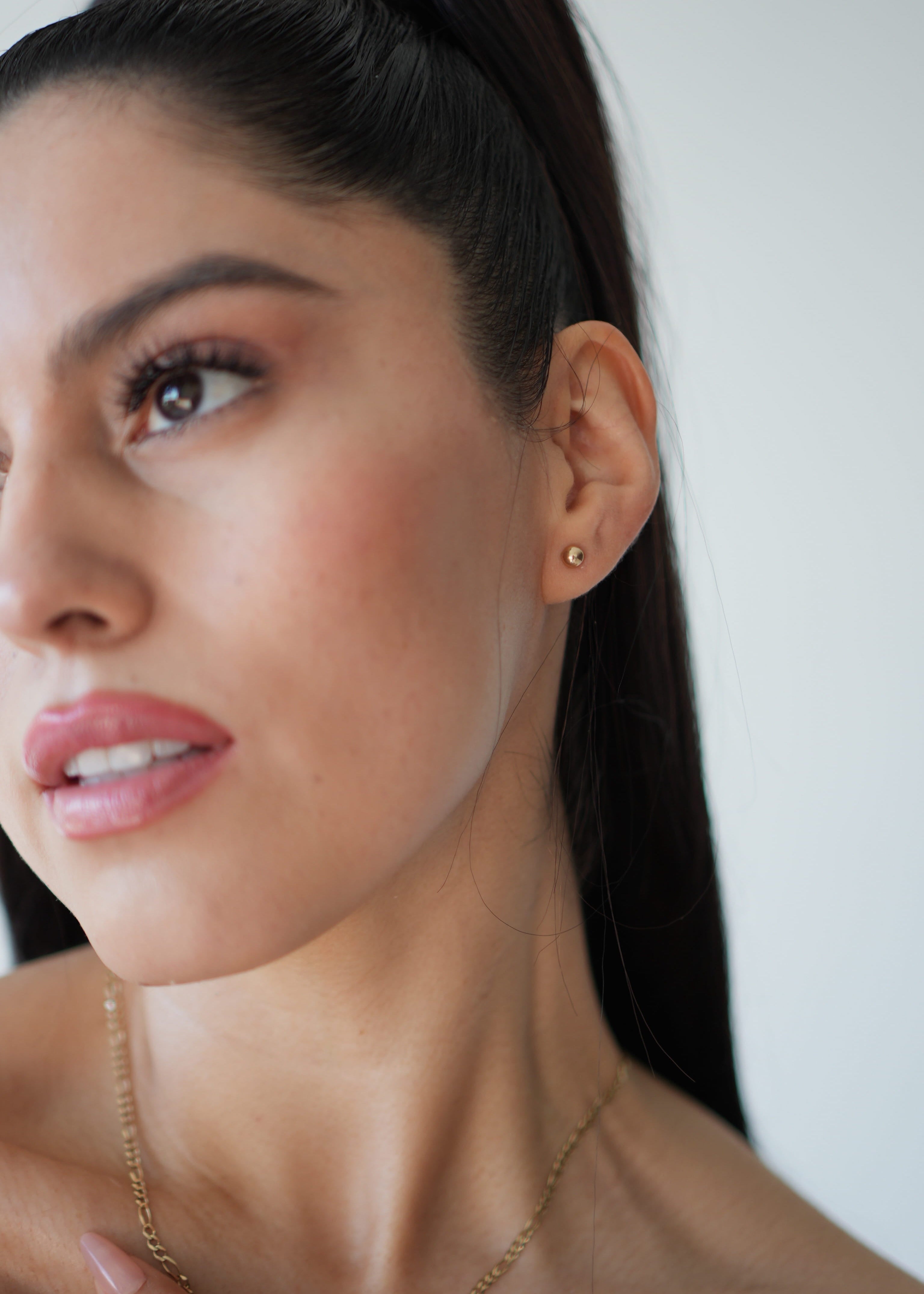 Close-up of a woman wearing a gold earring and necklace against a neutral background