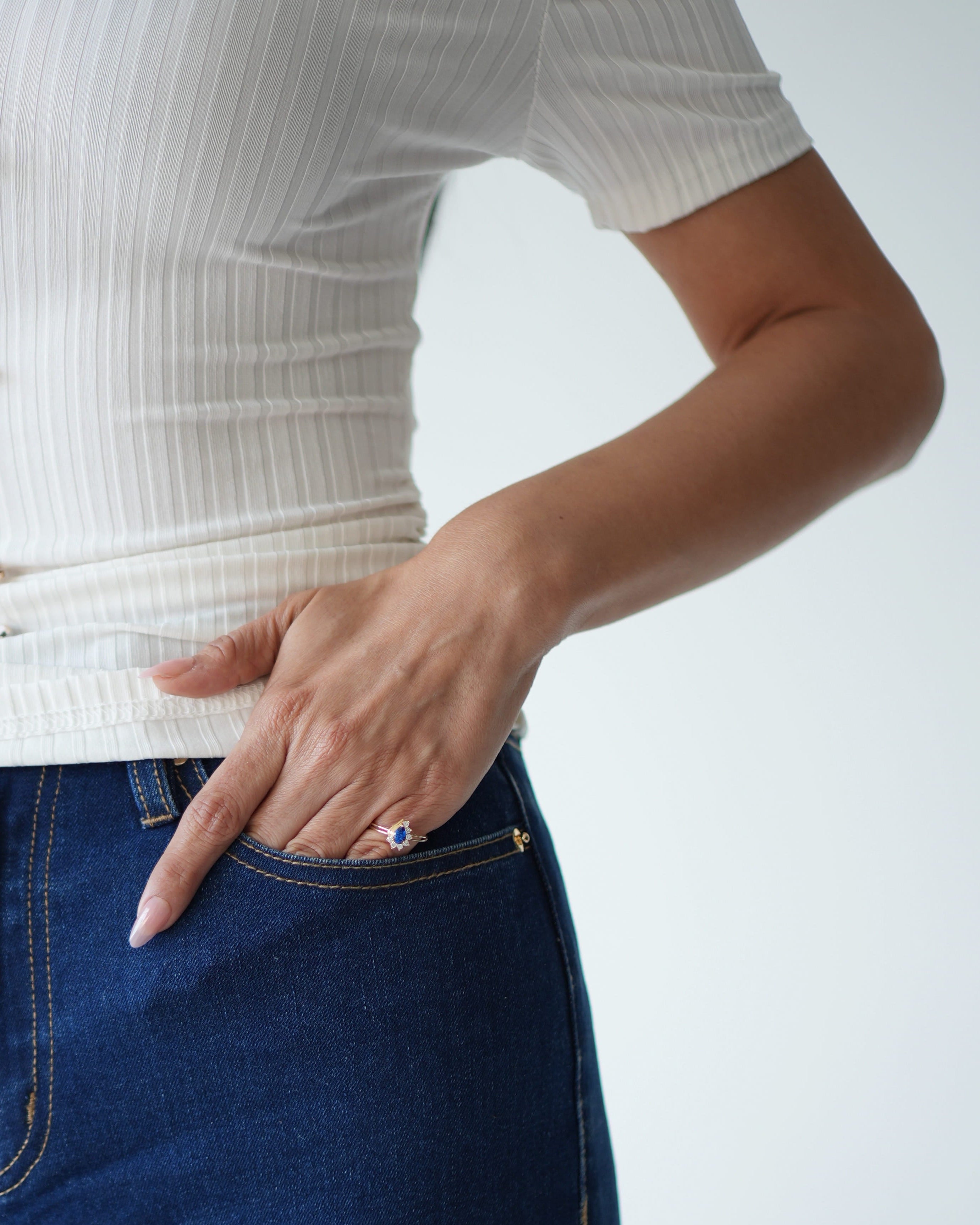 Person wearing a white ribbed top and blue jeans with a plain background