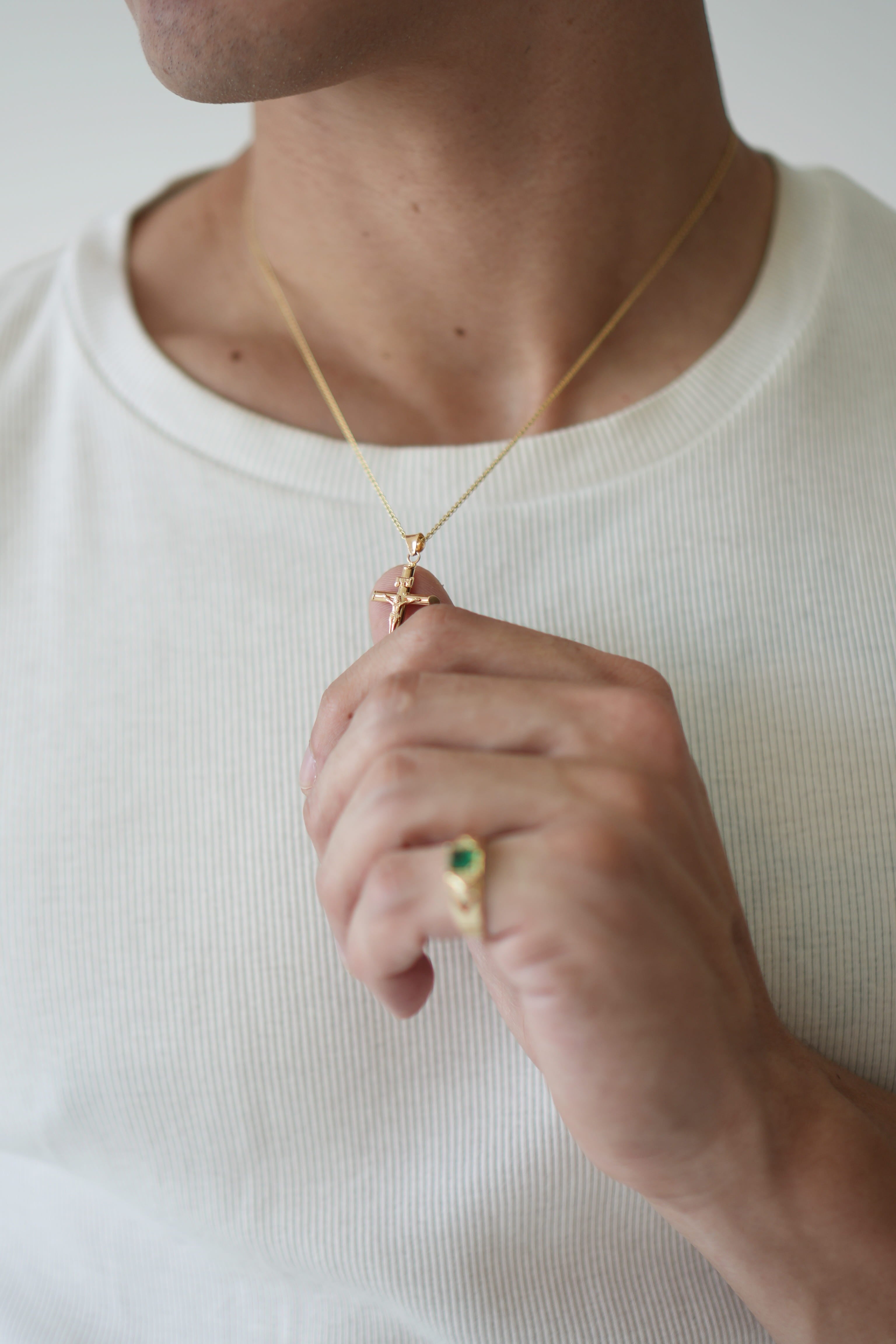 Person wearing a gold necklace and ring on a plain background