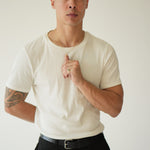 Man wearing a white t-shirt and black pants against a plain background