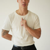 Man wearing a white t-shirt and black pants against a plain background