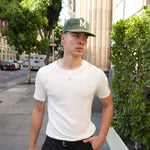 Man wearing a white t-shirt and green cap on a city street