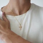 Person wearing a gold necklace with a cross pendant on a plain background
