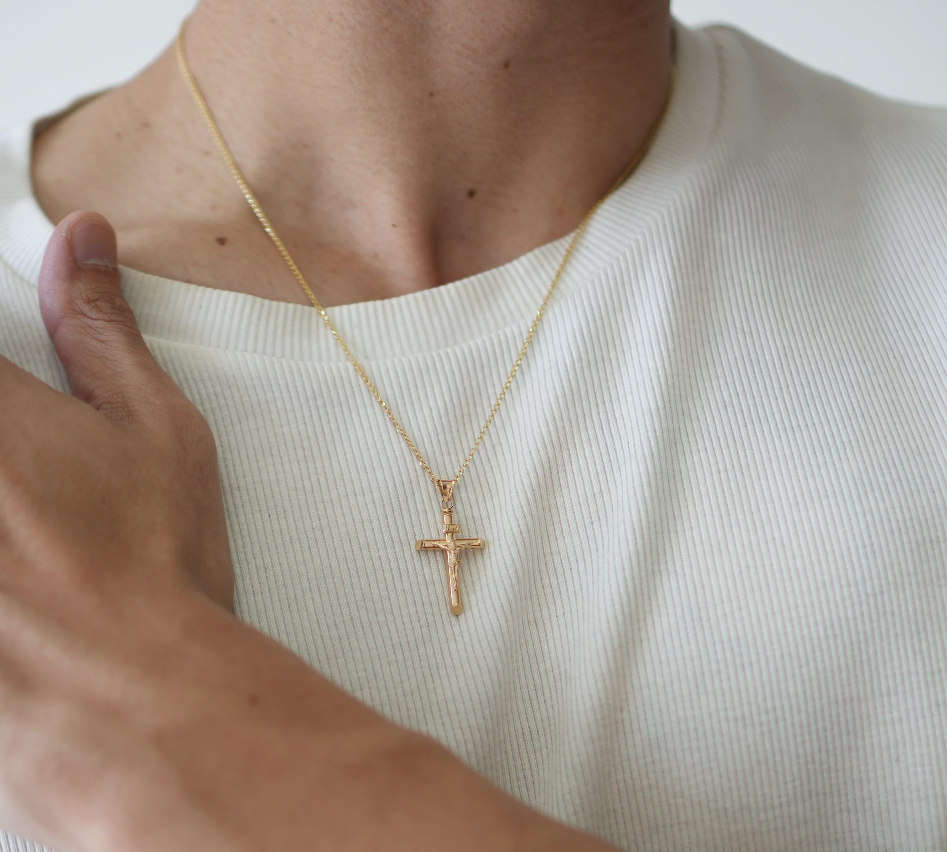 Person wearing a gold necklace with a cross pendant on a plain background