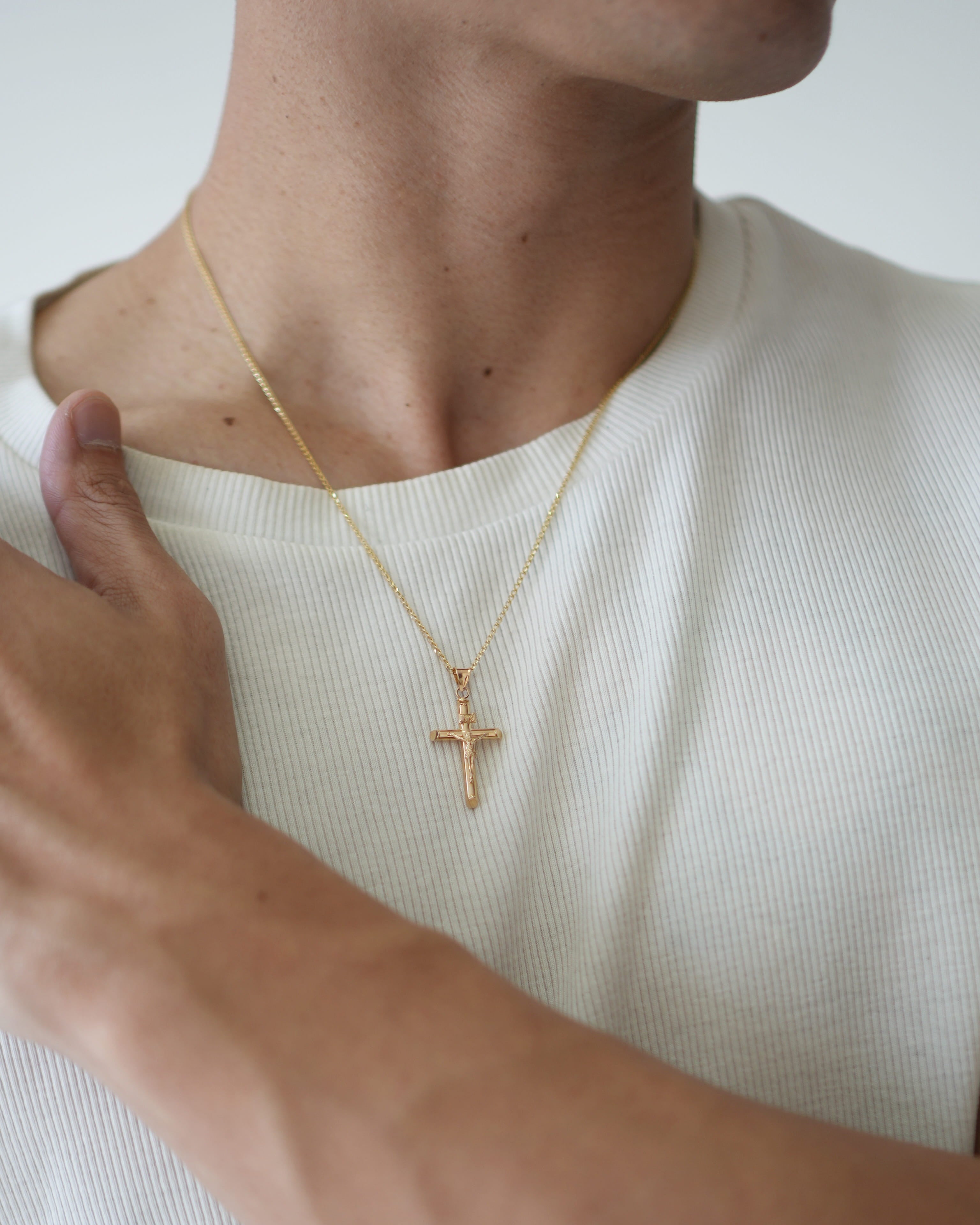 Person wearing a gold necklace with a cross pendant on a plain background