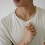 Man wearing a white t-shirt and gold necklace, holding a small object.