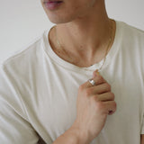 Man wearing a white t-shirt and gold necklace, holding a small object.