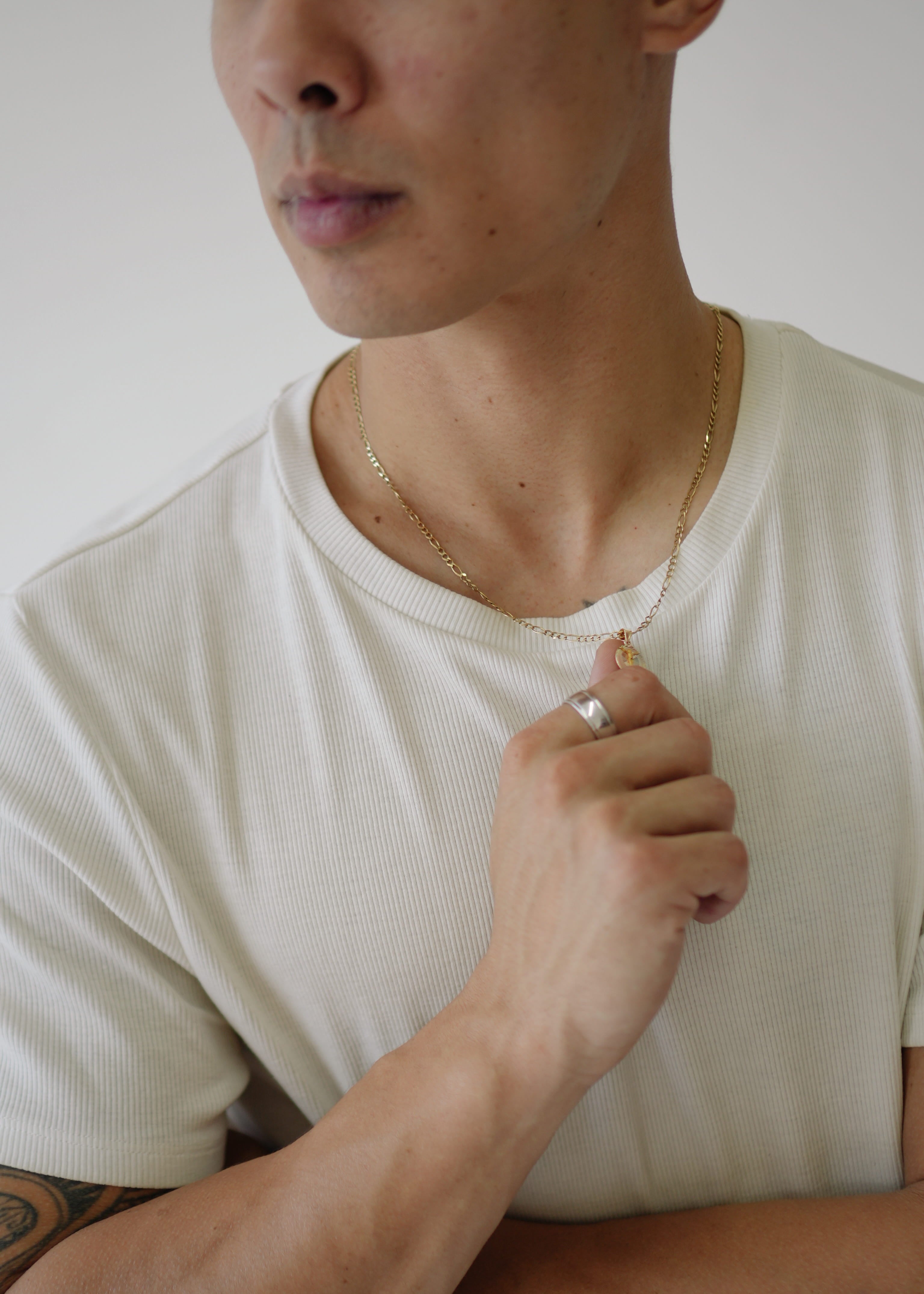 Man wearing a white t-shirt and gold necklace, holding a small object.