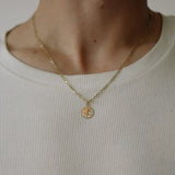 Gold necklace with a circular pendant worn by a person in a white shirt.