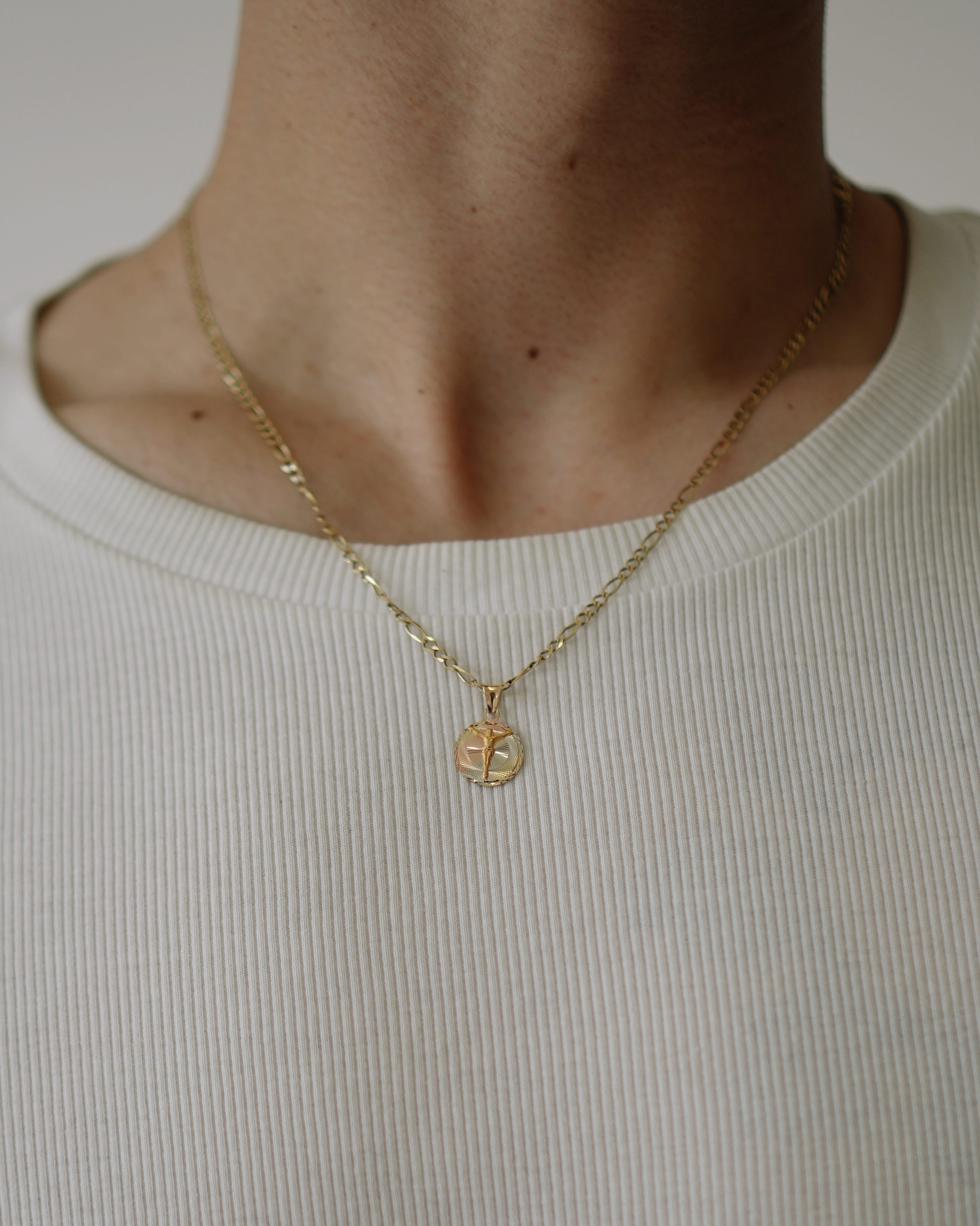 Gold necklace with a circular pendant worn by a person in a white shirt.