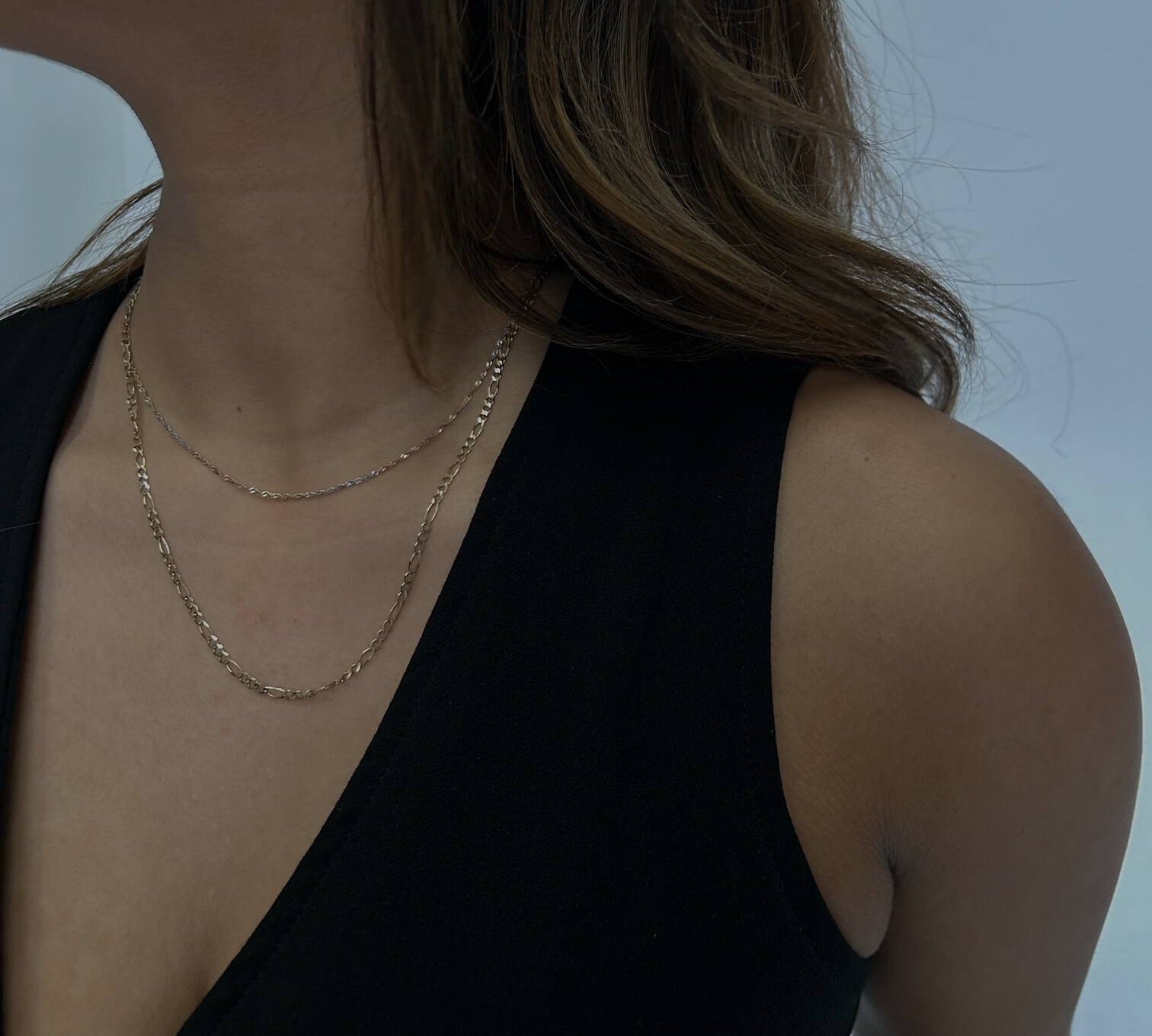 woman wearing a gold figaro chain against a white backdrop