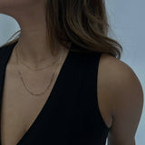 woman wearing a gold figaro chain against a white backdrop