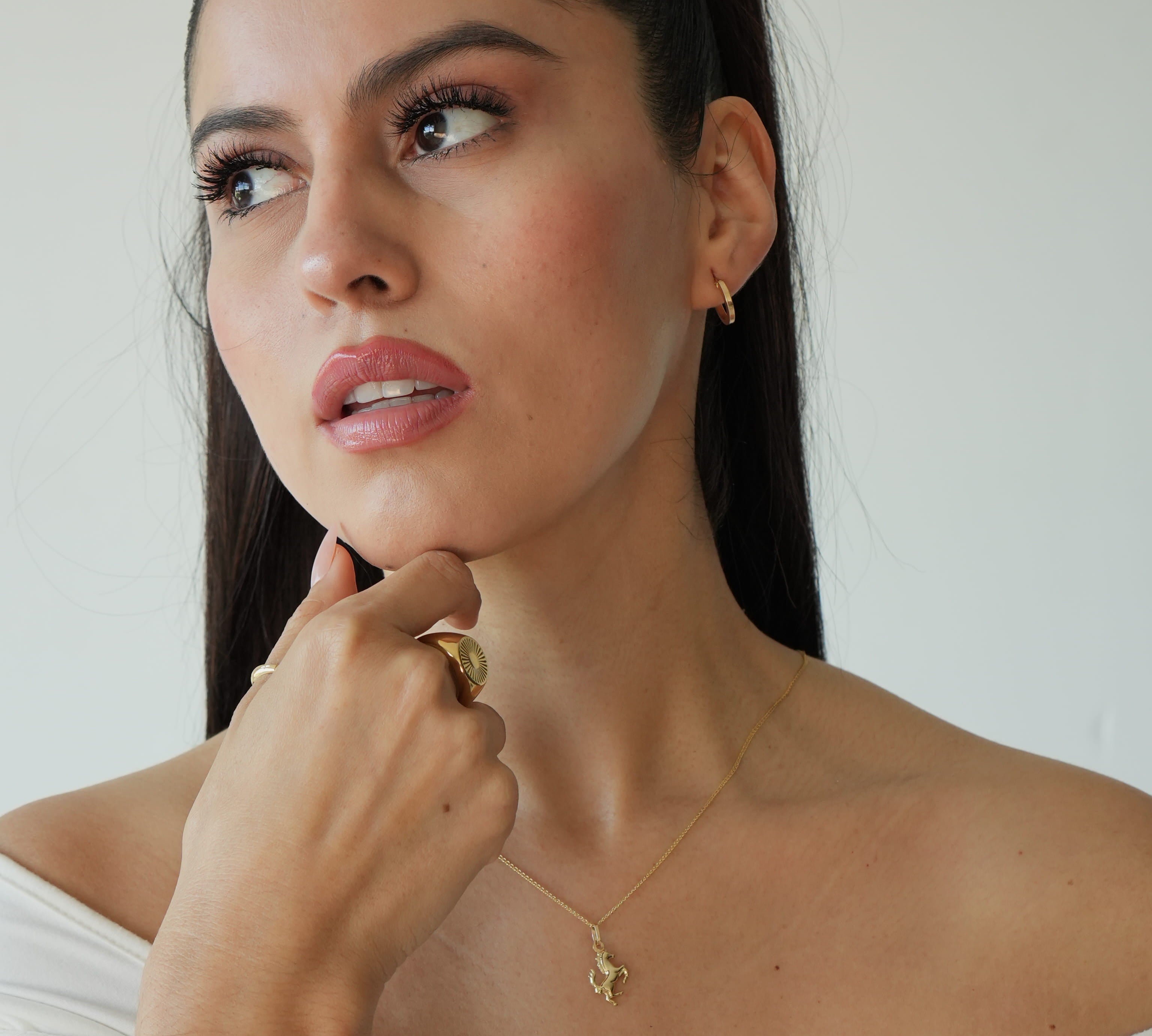 Woman wearing a gold necklace with a small pendant against a plain background