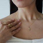 Close-up of a person wearing a gold necklace with a small pendant, hand resting on chest.