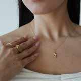 Close-up of a person wearing a gold necklace with a small pendant, hand resting on chest.