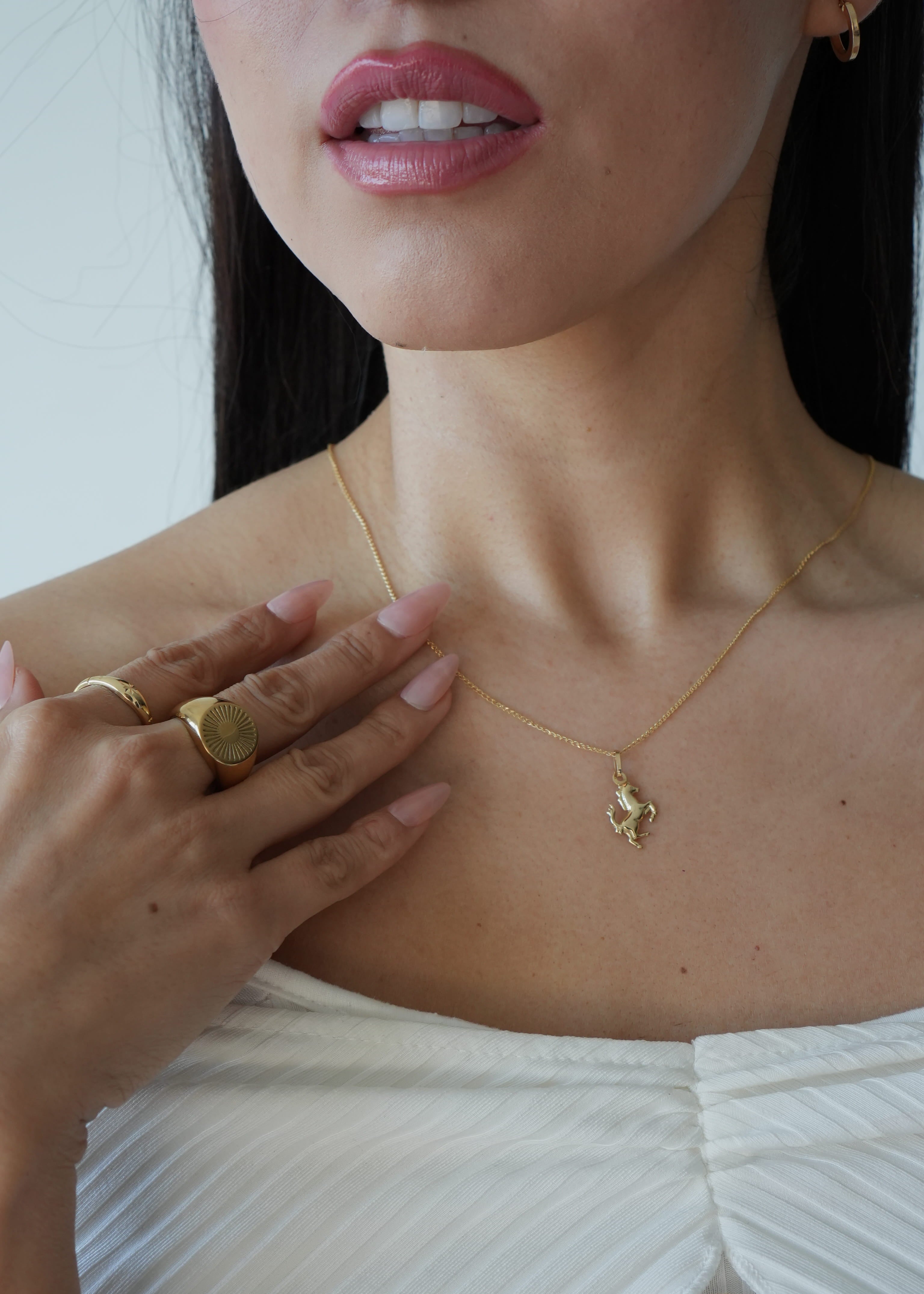 Close-up of a person wearing a gold necklace with a small pendant, hand resting on chest.