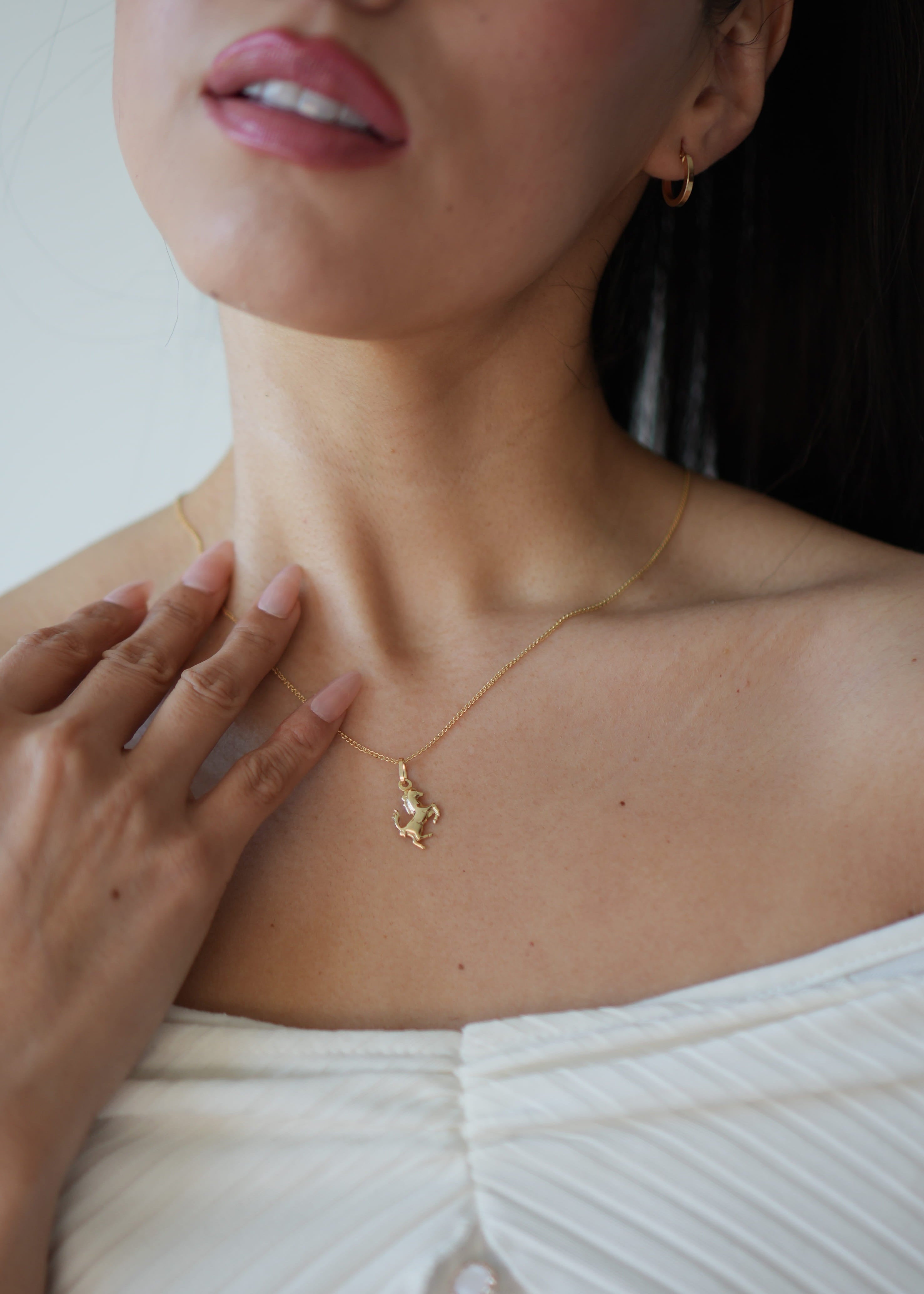 Woman wearing a gold necklace with a small pendant, close-up of neck and chest.