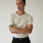 Man wearing a white t-shirt and black pants against a plain background