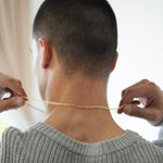 Person wearing a gray sweater and holding a gold chain around their neck.