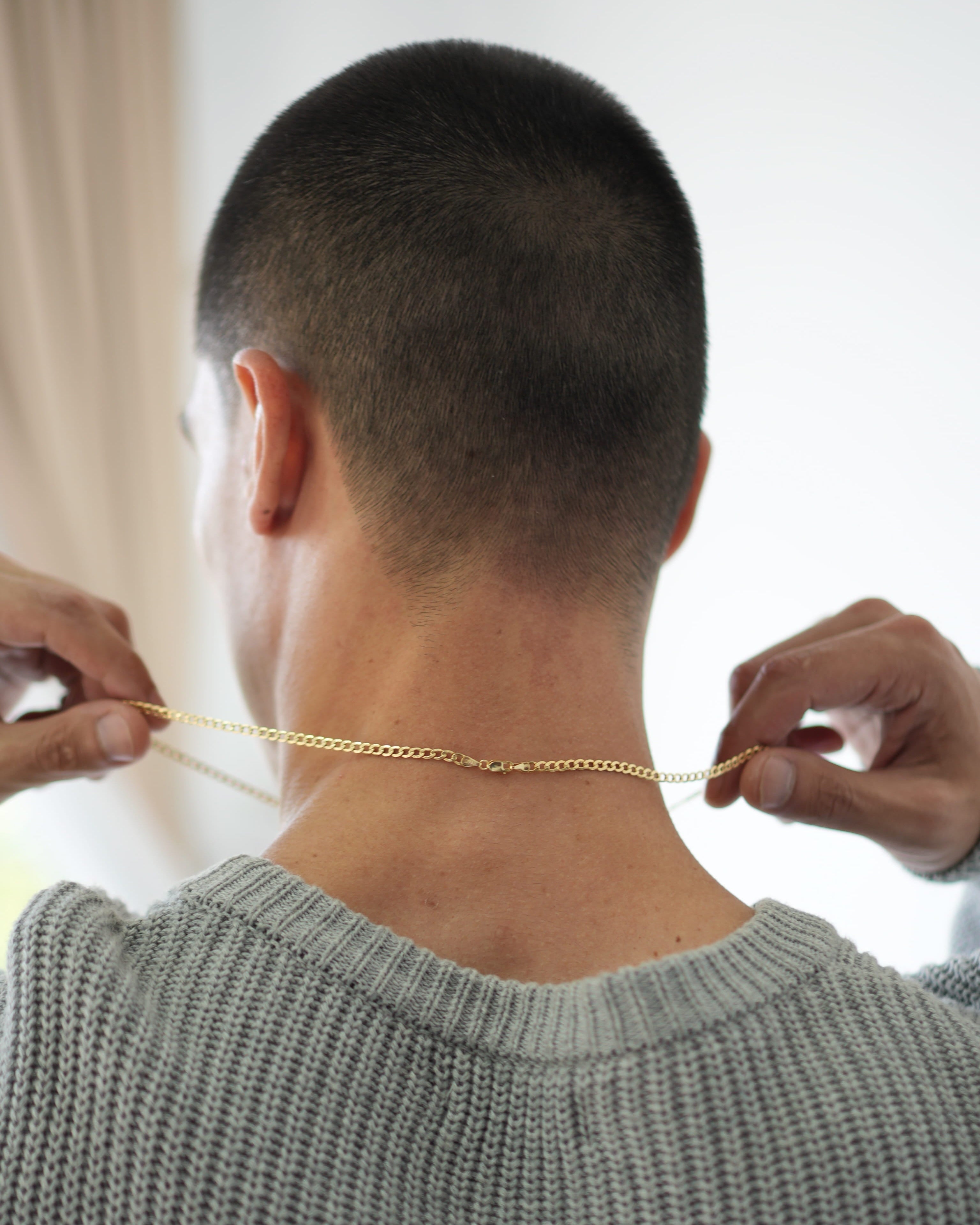Person wearing a gray sweater and holding a gold chain around their neck.