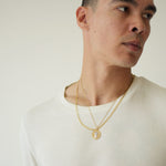 Man wearing a white shirt and gold necklace against a plain background