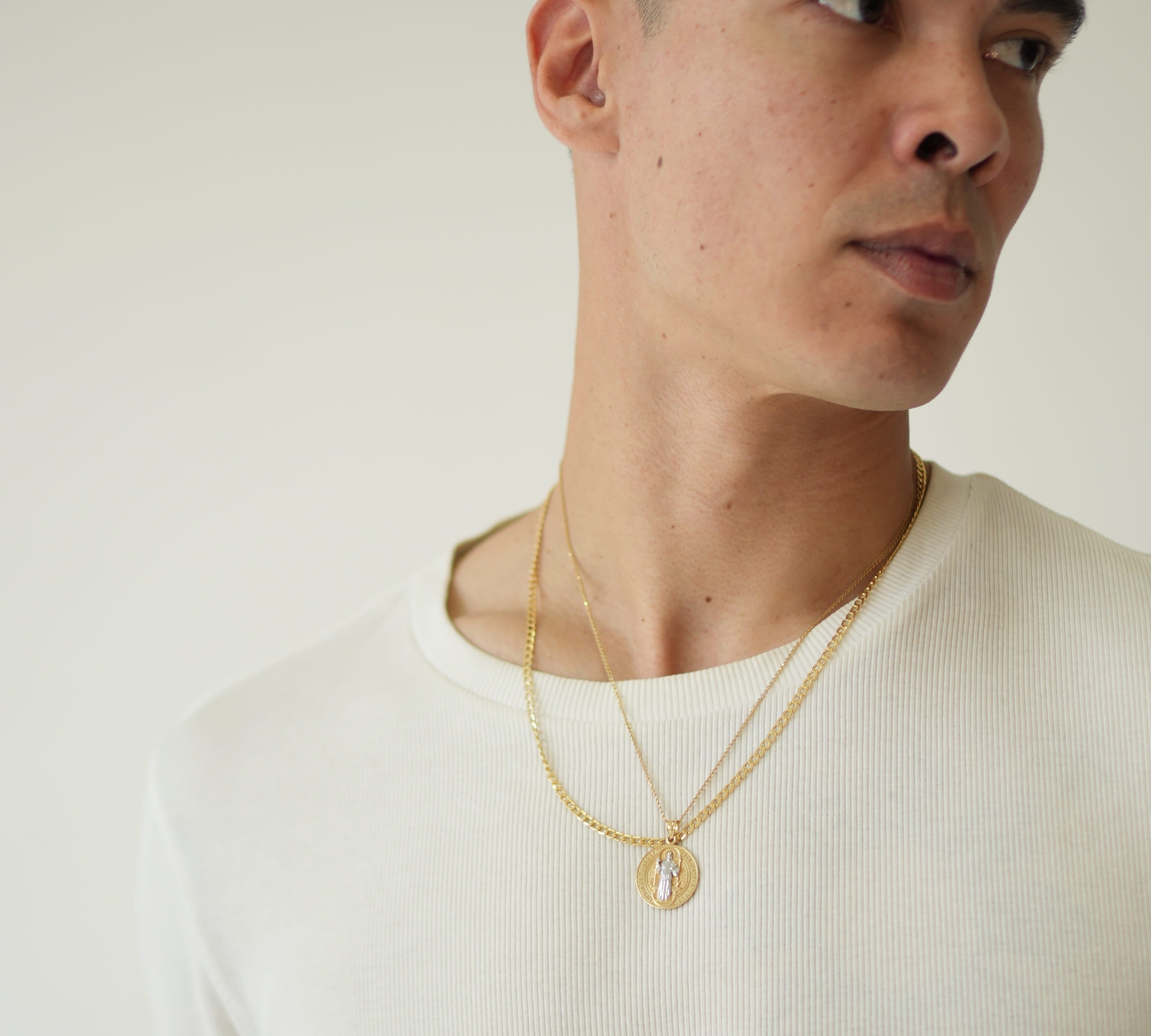 Man wearing a white shirt and gold necklace against a plain background