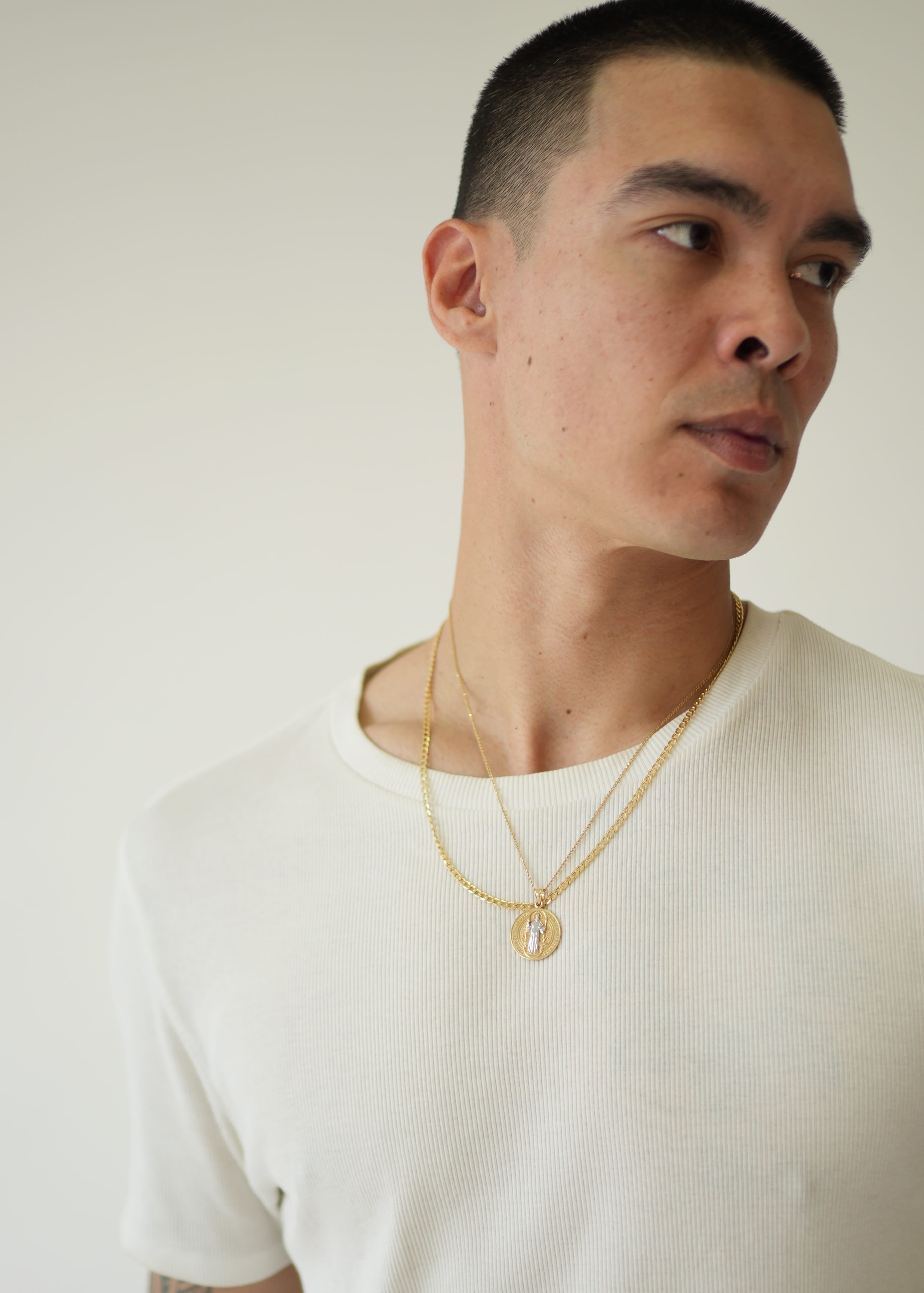 Man wearing a white shirt and gold necklace against a plain background