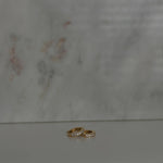 image of two gold earrings on top of each other against a marble backdrop
