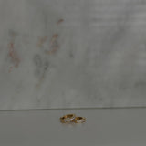 image of two gold earrings on top of each other against a marble backdrop