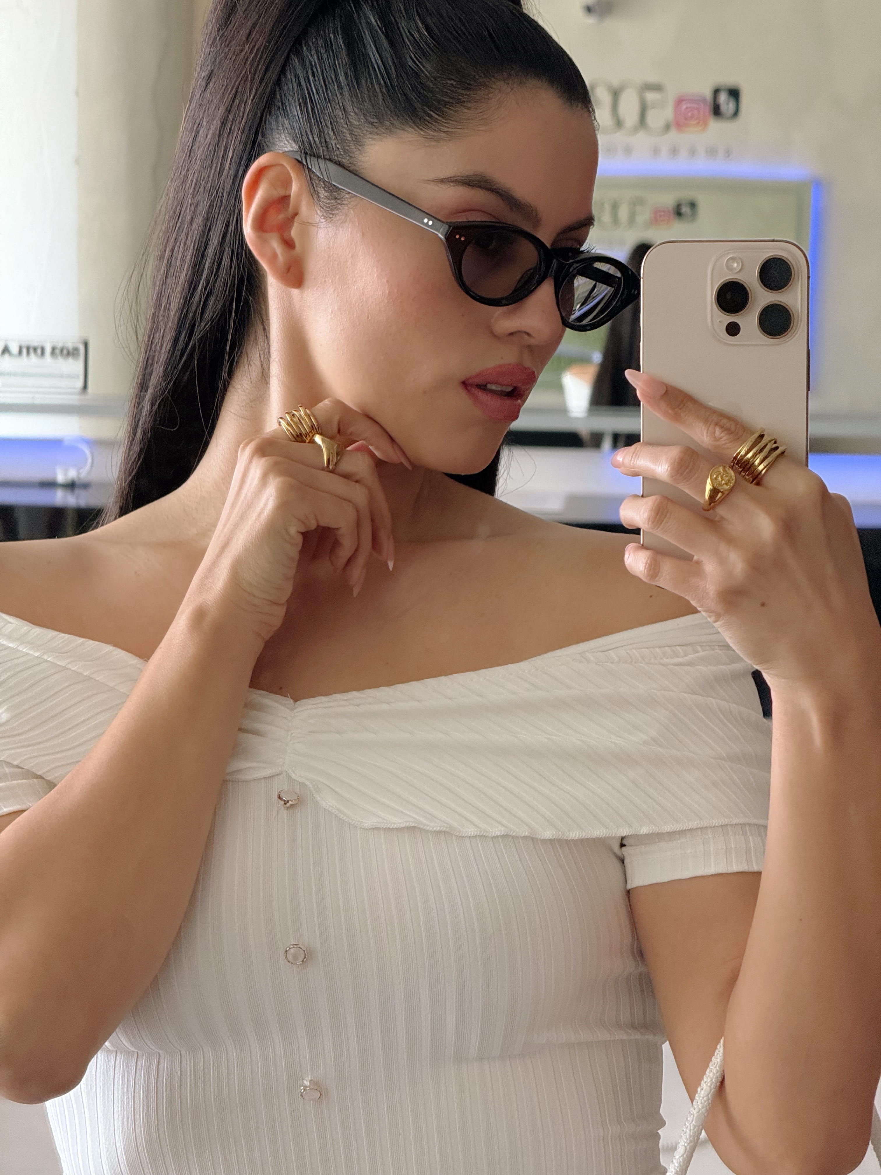 Woman in a white off-shoulder top taking a mirror selfie.