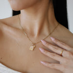 Close-up of a person wearing a gold necklace with a pendant, hand resting on chest.