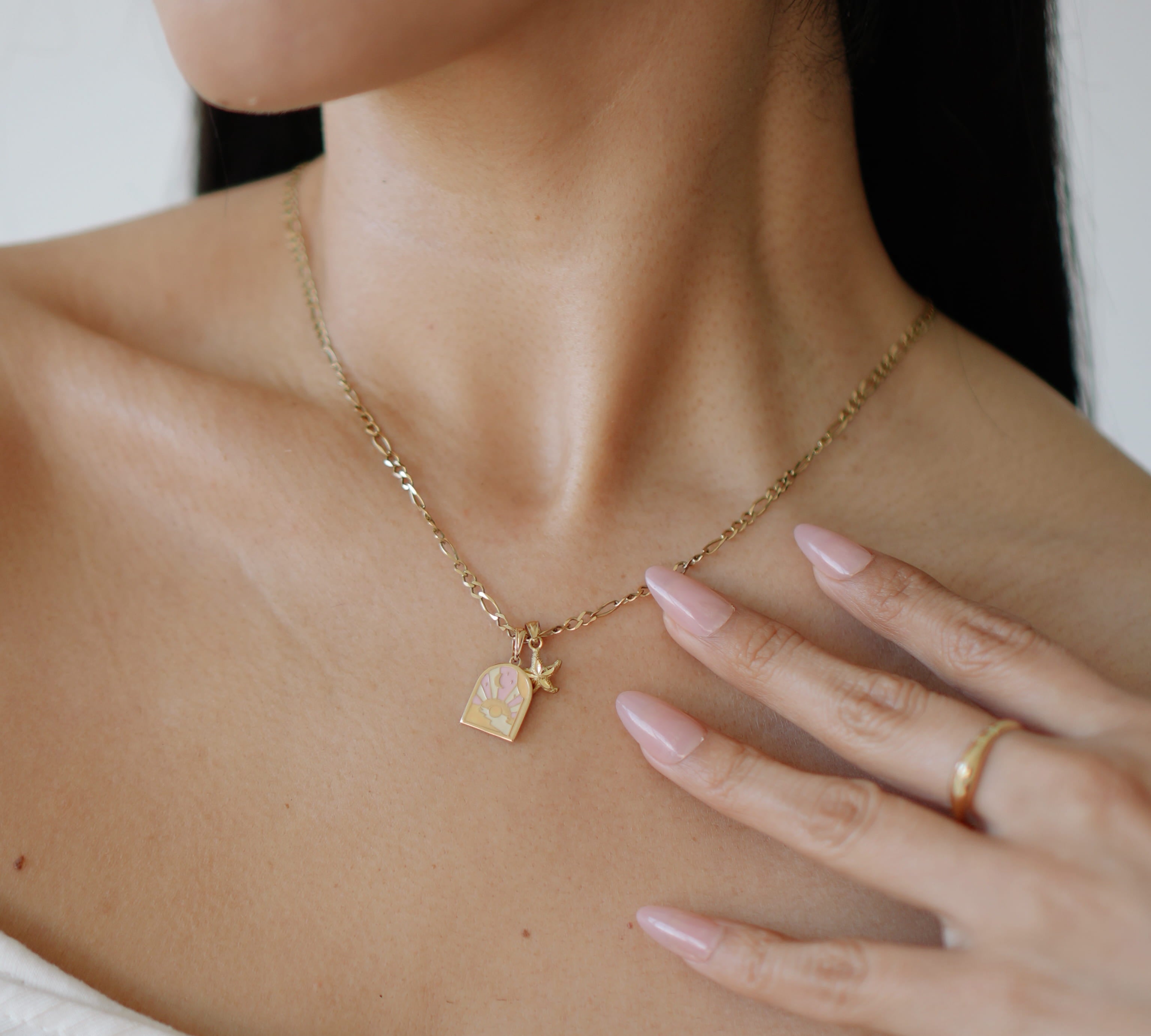 Close-up of a person wearing a gold necklace with a pendant, hand resting on chest.