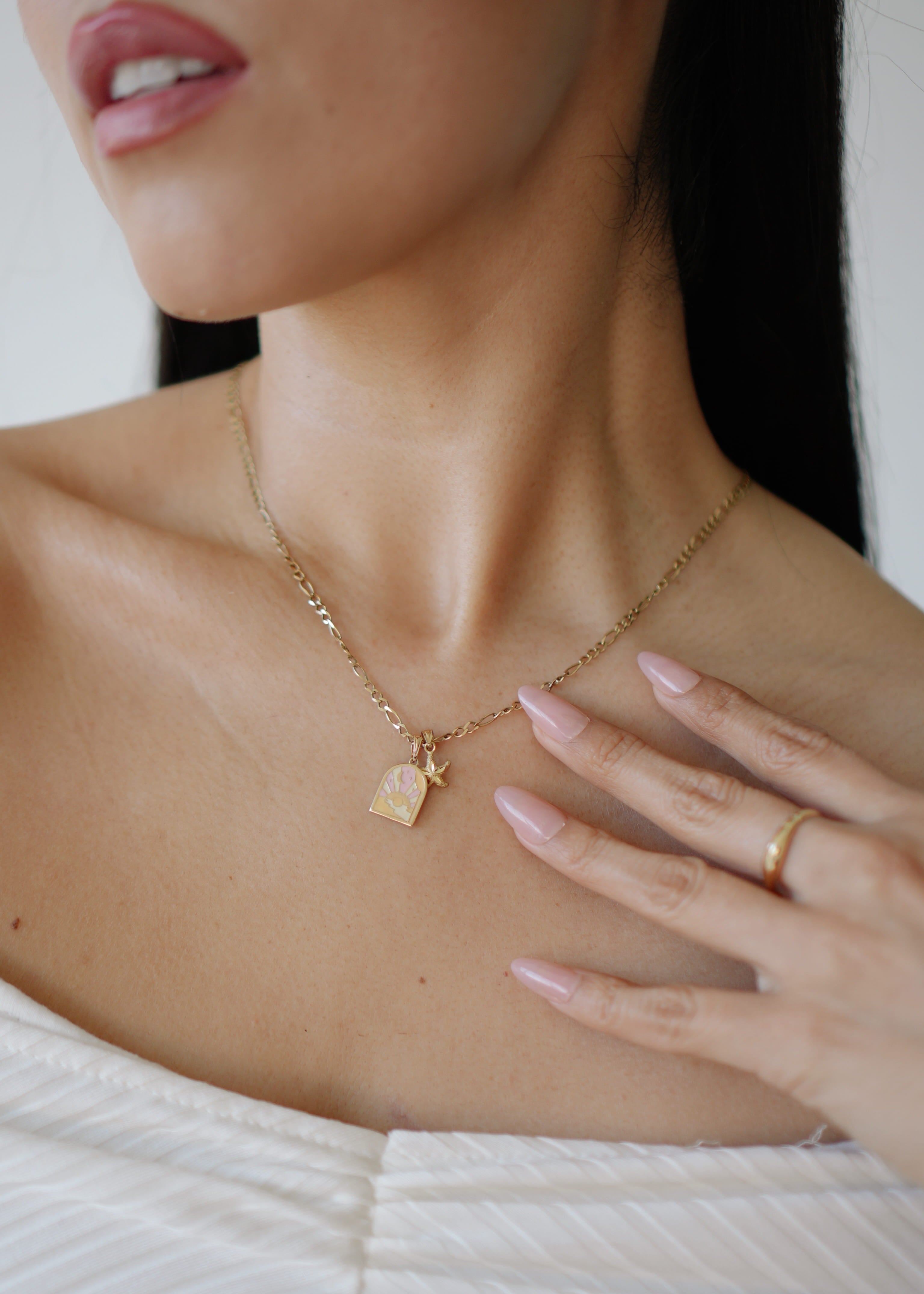 Close-up of a person wearing a gold necklace with a pendant, hand resting on chest.