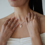 Woman wearing a gold necklace with a small pendant, touching her neck and shoulders.