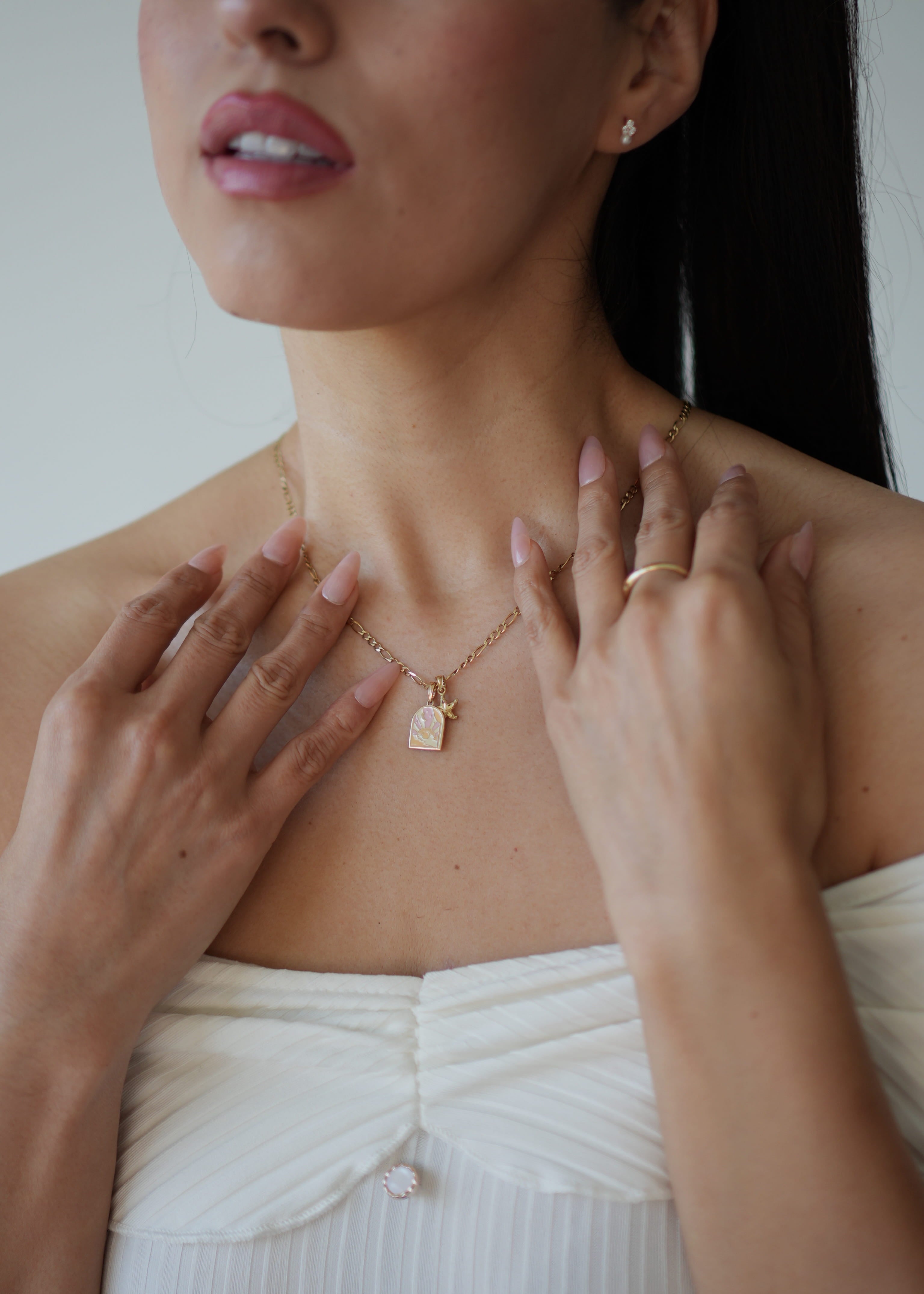 Woman wearing a gold necklace with a small pendant, touching her neck and shoulders.