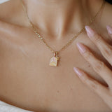 Gold necklace with a pendant worn by a person, with a hand touching the neck.