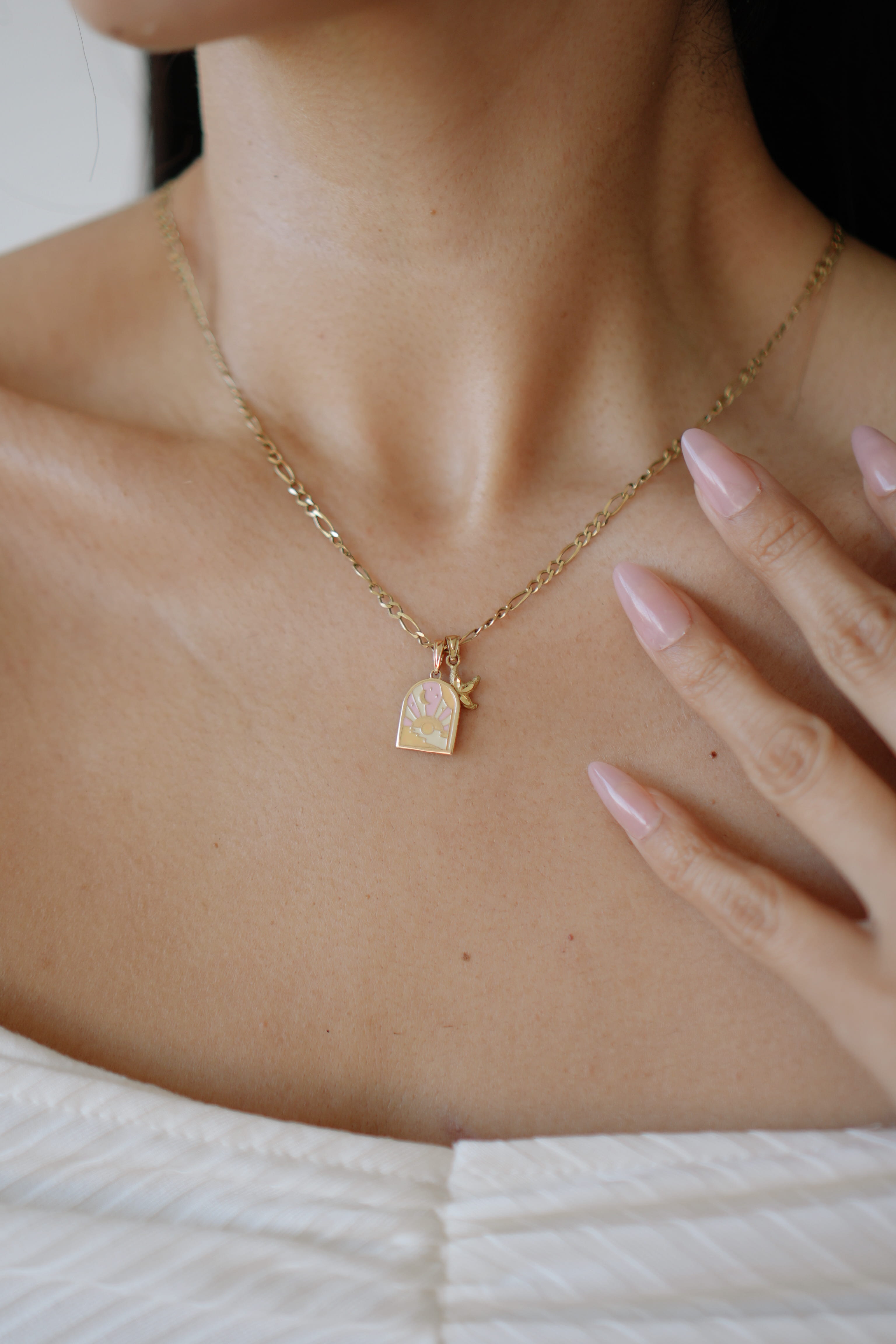 Gold necklace with a pendant worn by a person, with a hand touching the neck.