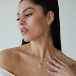 Woman wearing a gold necklace and ring, with a plain background