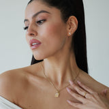Woman wearing a gold necklace and ring, with a plain background