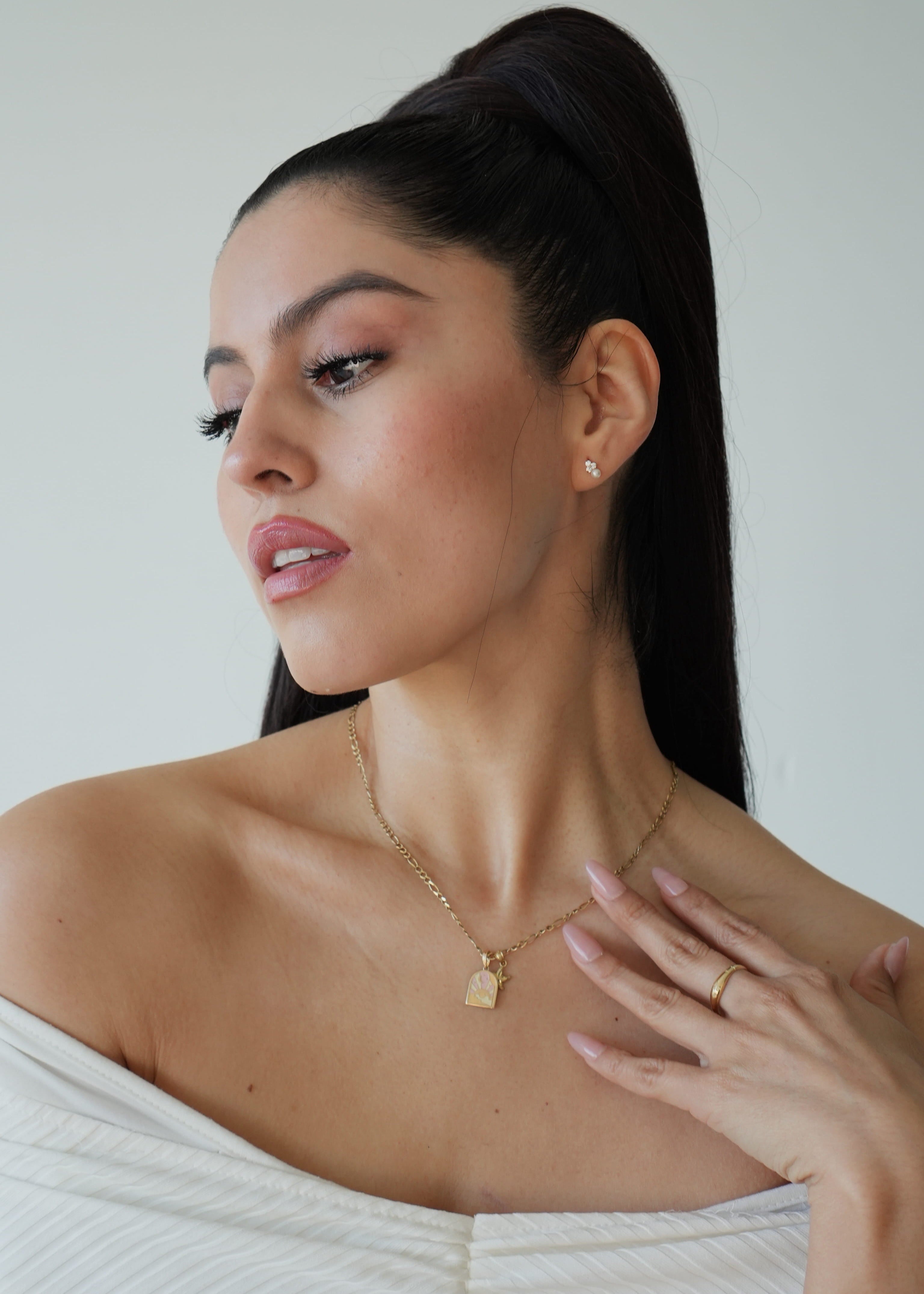Woman wearing a gold necklace and ring, with a plain background