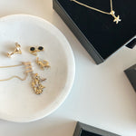 Gold earrings on a white dish with black jewelry boxes in the background