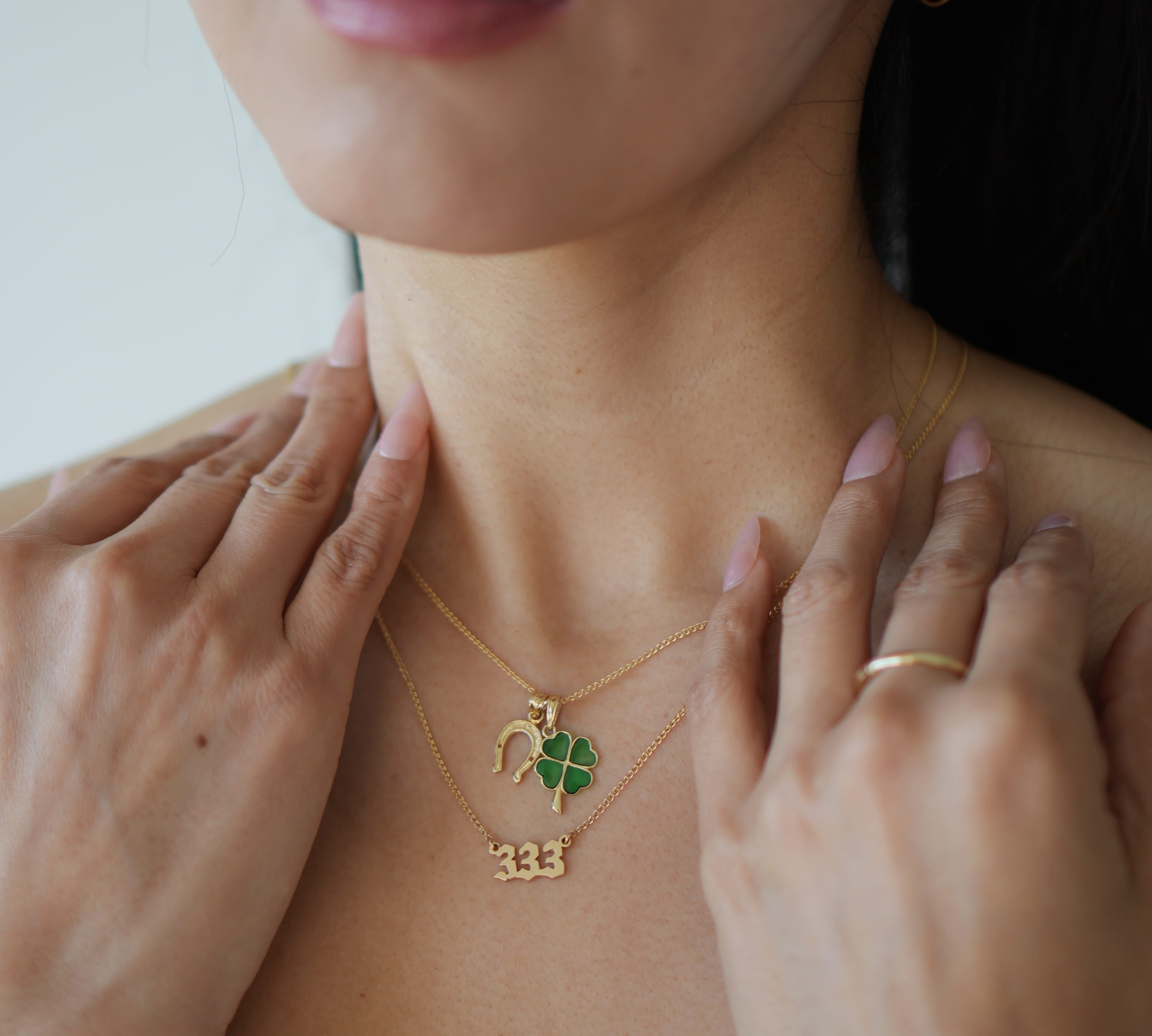 Close-up of a person wearing a gold necklace with a green pendant and number '333' on a plain background.