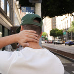 Person wearing a green cap and white shirt on a city street with a traffic light and buildings in the background.