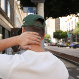 Person wearing a green cap and white shirt on a city street with a traffic light and buildings in the background.