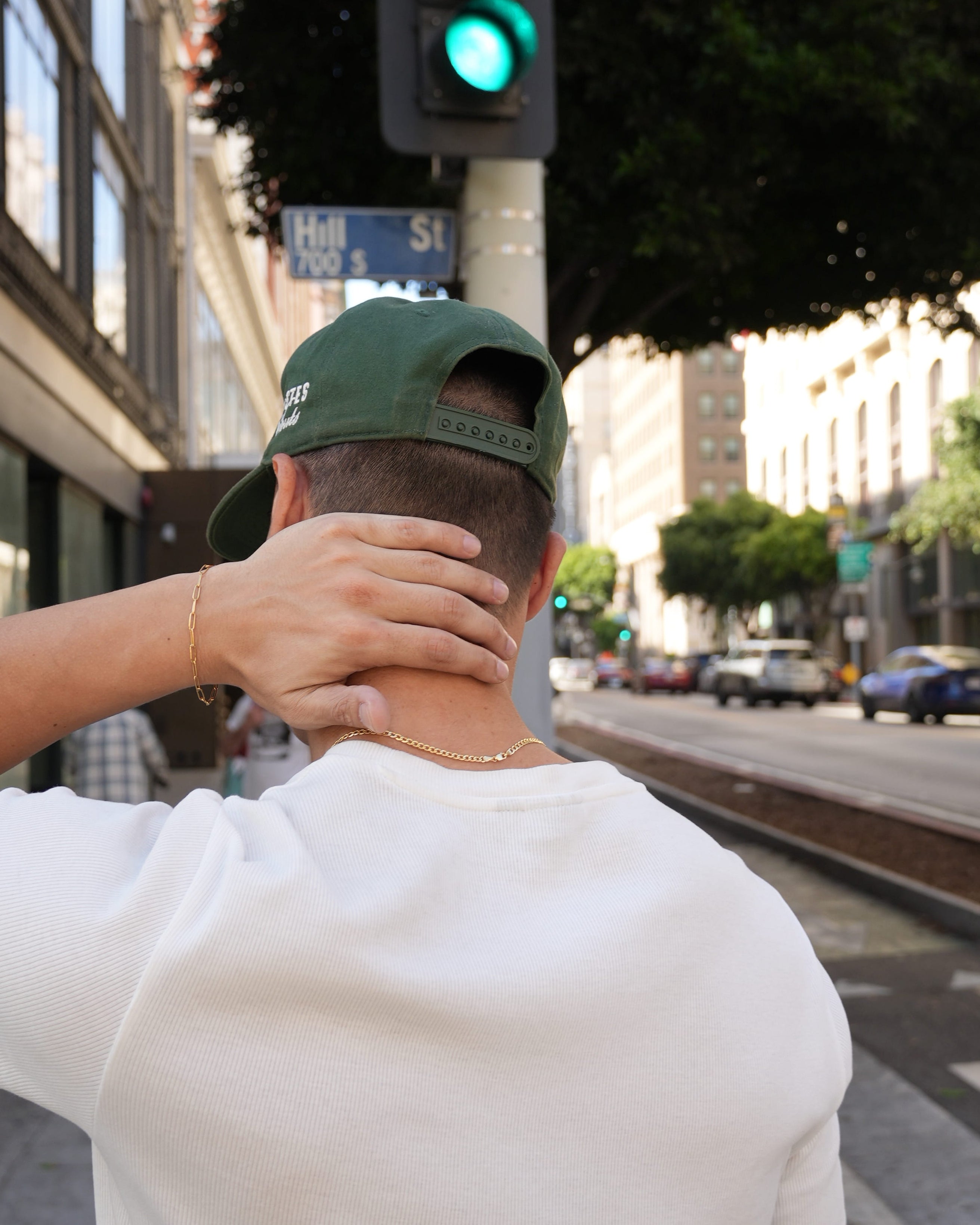 Person wearing a green cap and white shirt on a city street with a traffic light and buildings in the background.